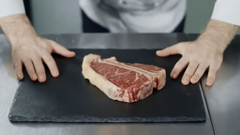 Chef-preparing-to-cook-at-kitchen-restaurant.-Closeup-chef-hands-with-raw-steak.