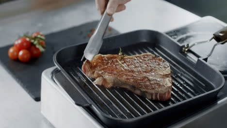 Chef-preparing-meat-at-griddle.-Closeup-chef-hands-turning-steak-with-tongs.