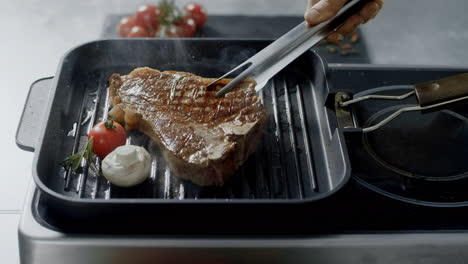 Chef-cooking-steak-at-griddle-pan.-Closeup-man-hands-turning-steak-with-tongs.