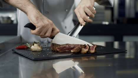 Chef-hands-cutting-steak-at-kitchen-restaurant.-Closeup-chef-slicing-meat
