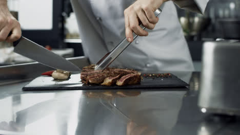 Male-chef-cutting-steak-at-kitchen-restaurant.-Closeup-chef-hands-cutting-meat