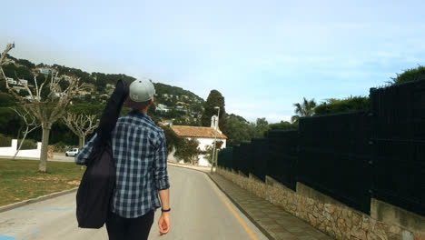 Guy-walking-on-road-with-guitar-gig-bag.-Back-view-musician-boy-traveling