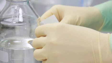 Laboratory-worker-sticking-sticker-at-bottle-with-transparent-liquid