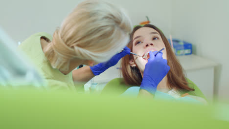 Dental-technician-examining-patient-teeth-with-dental-instruments