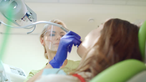 Female-dentist-treating-patient-teeth.-Blonde-doctor-in-protective-goggles