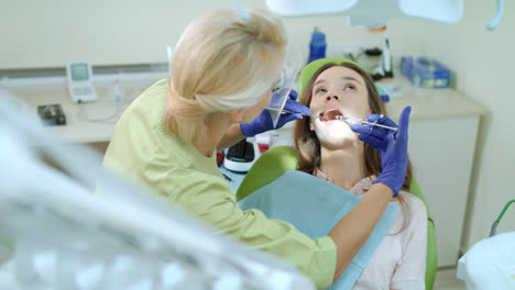 Female-dentist-using-mouth-mirror-and-medicine-syringe.-Doctor-treating-patient
