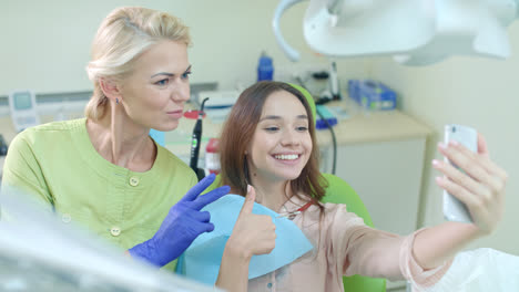 Smiling-doctor-and-patient-taking-selfie-in-dentist-office.-Woman-showing-v-sign