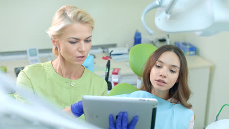 Female-dentist-using-tablet-computer.-Dentist-showing-patient-treatment-plan