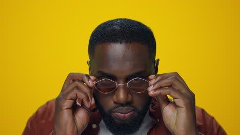 Portrait-of-serious-african-man-putting-sunglasses-in-yellow-background.