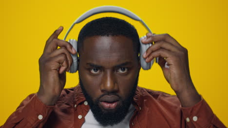 Portrait-of-surprised-african-guy-listening-music-on-headphones-in-studio.