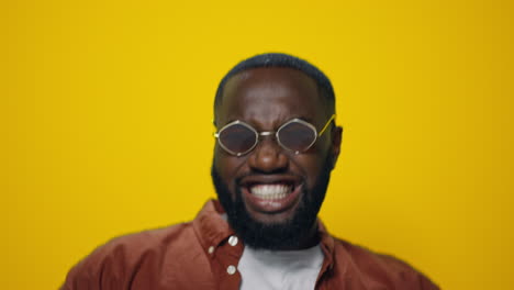 Closeup-positive-african-american-guy-in-sunglasses-dancing-in-yellow-background