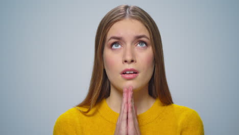 Portrait-of-attractive-young-woman-praying-at-camera-on-grey-background.