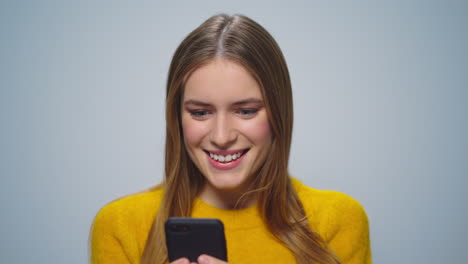 Portrait-of-surprised-woman-reading-good-news-in-smartphone-on-grey-background.