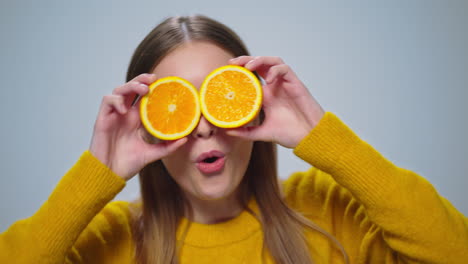 Portrait-of-cheerful-woman-having-fun-with-two-orange-slices-in-studio.