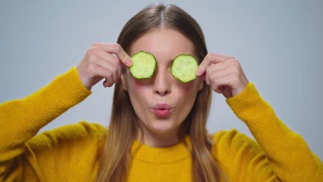 Portrait-of-smiling-woman-having-fun-with-two-cucumber-slices-in-studio.