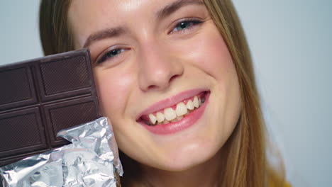 Closeup-young-woman-looking-with-chocolate-bar-at-camera-ion-grey-background.