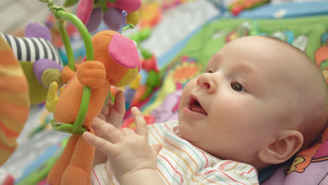 Cute-infant-have-fun-with-toys.-Close-up-of-happy-baby-lying-on-developing-mat