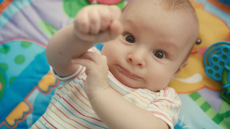 Portrait-of-infant-looking-at-camera-on-colored-mat.-Close-up-of-cute-baby-face
