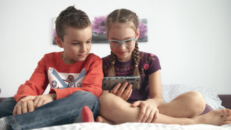 Brother-and-sister-watching-cartoons-on-mobile-phone-at-home