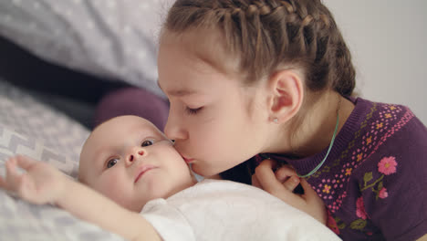 Beautiful-girl-kissing-baby-lying-on-sofa.-Sister-kiss-newborn-brother
