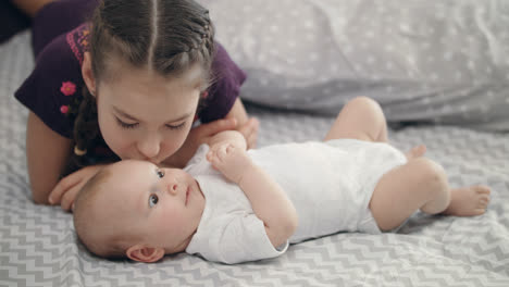 Mädchen-Küsst-Neugeborenes-Baby,-Das-Auf-Dem-Rücken-Liegt.-Schwesterliebe-Konzept