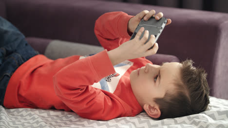 Boy-playing-mobile-game-on-smartphone-on-sofa.-Kid-playing-mobile-phone