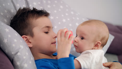 Close-up-of-older-brother-playing-with-baby-boy-on-bed.-Child-love-concept
