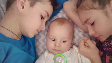 Siblings-with-baby-on-bed.-Close-up-of-brother-and-sister-kiss-newborn-baby-boy