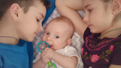 Siblings-kissing-newborn-brother.-Boy-and-girl-care-baby-Concept-of-kids-love