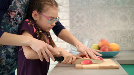 Woman-help-child-to-cut-apple-slice.-Mother-and-daugther-cooking-together
