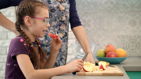 Girl-eating-apple-slice-on-kitchen.-Child-eating-fruit-with-mother-on-kitchen
