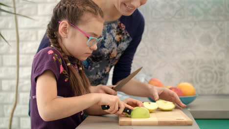 Mother-learning-daughter-to-use-knife.-Mom-and-child-cut-apple-slice-together