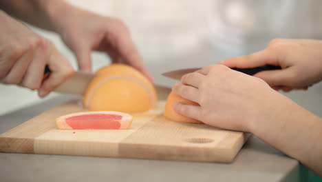 Mother-hand-cutting-grapefruit-slice.-Woman-and-kid-hands-cutting-citrus-fruit