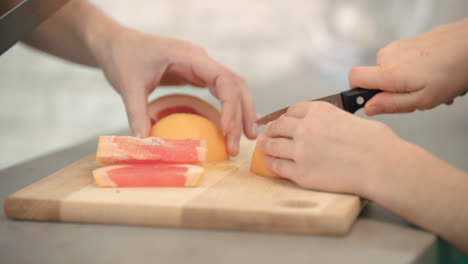 Cooking-hands-cutting-fruit.-Grapefruits-sliced-on-wooden-board