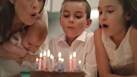 Happy-family-birthday-party-at-home.-Family-blowing-candle-flames-on-party-cake