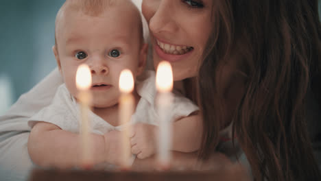 Mom-with-baby-blowing-birthday-candle.-Woman-with-kid-blowing-candles-on-cake
