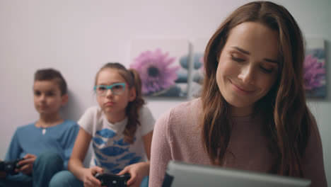 Glückliche-Mutter-Schaut-Zu-Hause-Auf-Ein-Tablet,-Während-Kinder-Videospiele-Spielen