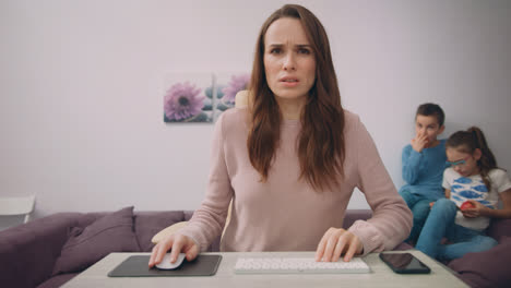 Unhappy-mother-working-on-computer-at-home-with-kids.-Concentrated-woman