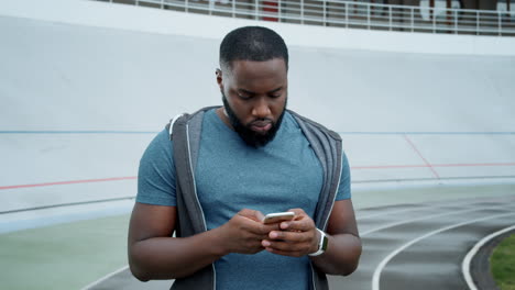 Athlete-using-smartphone-at-stadium.-Sportsman-texting-message-on-smartphone