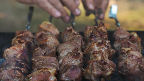 Bbq-meat-grilling-on-open-grill-outdoor.-Close-up-male-hand-turning-meat-skewers