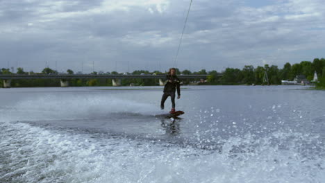 Man-riding-wakeboard-on-wave-of-motorboat-in-summer-river.-Active-life