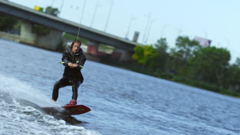 Young-man-riding-wakeboard-on-summer-river.-Waterskier-moving-fast-in-splashes