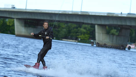 Energy-sportsman-in-black-swimsuit-wakeboarding.-Wakeboarder-surfing-across-lake