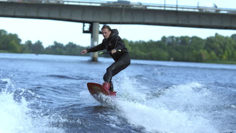 Man-wakeboarding-on-river-waves-under-city-bridge-in-slow-motion