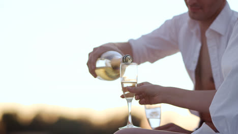 Handsome-man-pouring-champagne-in-wineglasses.-Love-couple-relaxing-outdoor