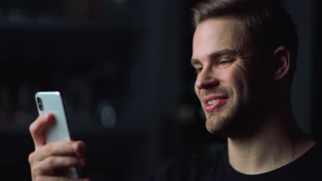 Side-portrait-smiling-caucasian-guy-making-video-calling-on-smartphone-indoors.