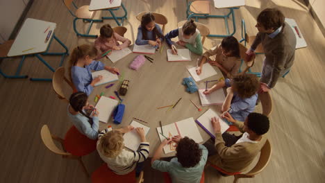Schoolchildren-having-lesson-at-round-table.-Male-teacher-helping-kids-at-lesson