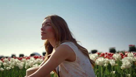 Thoughtful-girl-sitting-in-flower-field-in-sunlight.-Woman-dreaming-among-tulips