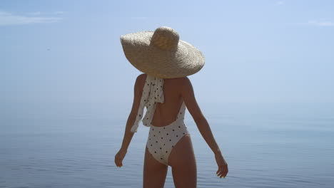 Relaxed-girl-standing-beach-raising-hands-to-brimmed-hat-close-up.-Woman-relax.