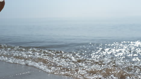 Tanned-woman-legs-splashing-ocean-waves-on-sunlight-close-up.-Girl-feet-walking.
